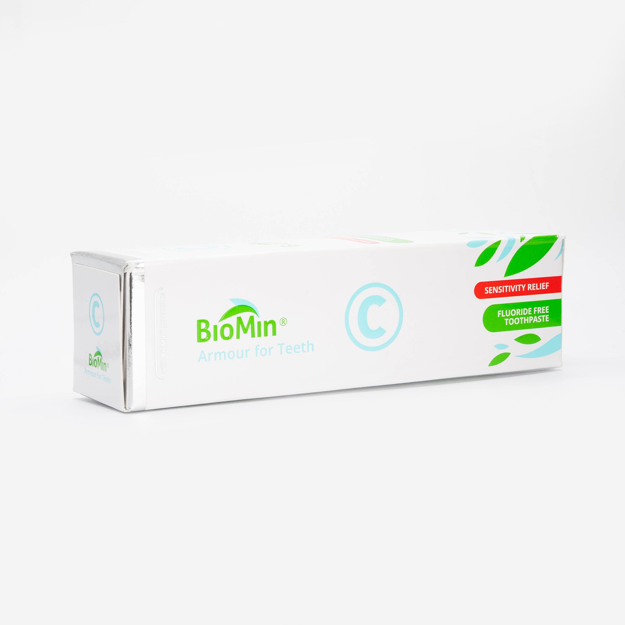A white box of BioMin C toothpaste, lied horizontally, labeled "Armour for Teeth" with fluoride free protection. The box features green leaf designs and a prominent blue "C" symbol, indicating fluoride free content.