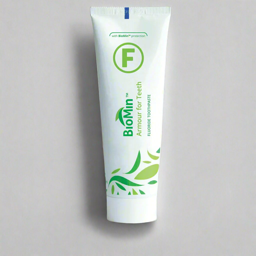 A white tube of BioMin F toothpaste labeled "Armour for Teeth" with fluoride protection. The tube features green leaf designs and a prominent green "F" symbol, over a white background, indicating fluoride content.
