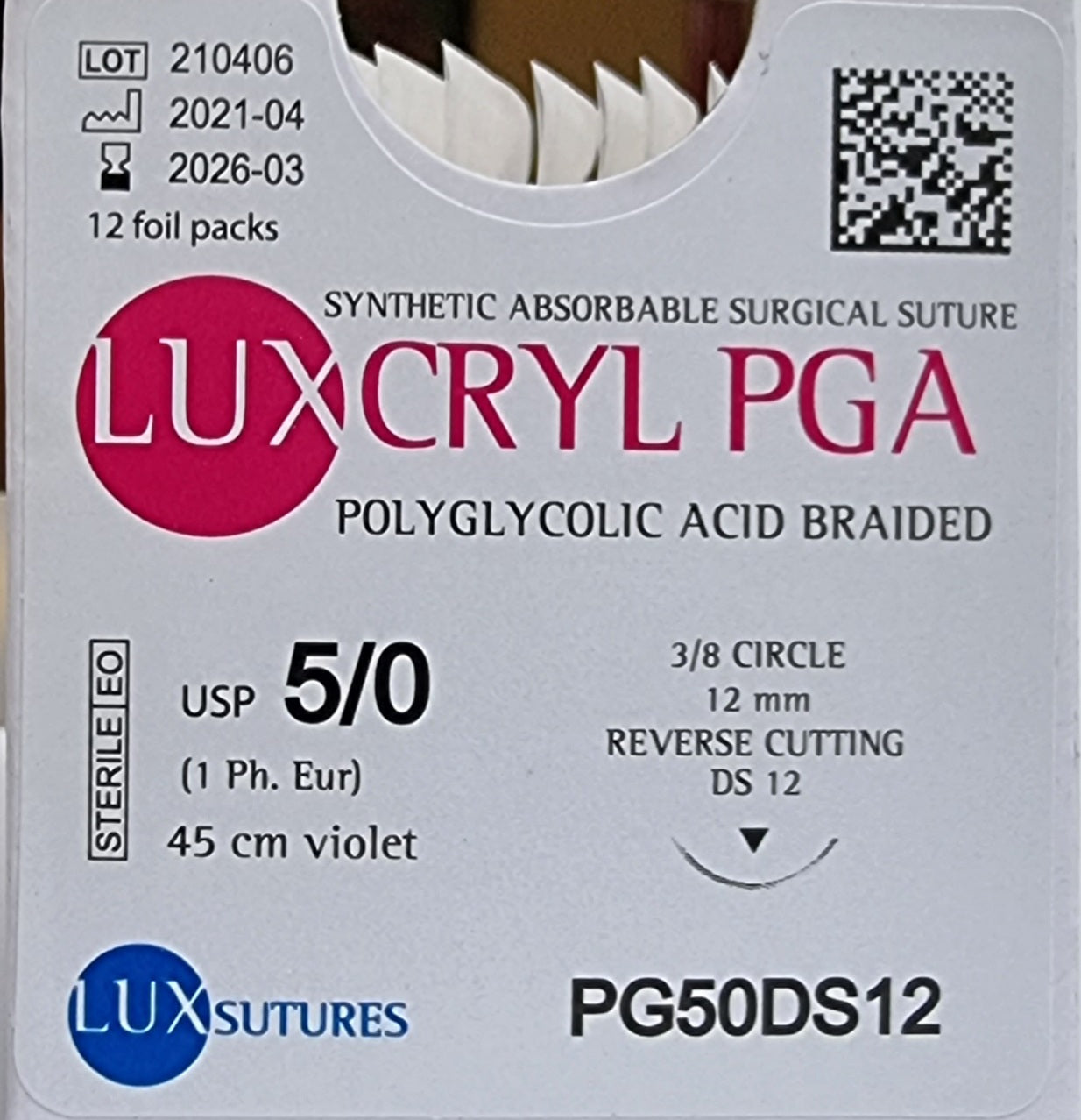 A close-up view of the front of a Luxcryl PGA synthetic absorbable surgical suture box. The label specifies USP 5/0 (1 Ph. Eur.), 45cm violet suture, and a 12mm 3/8 circle reverse cutting needle. The product is described as polyglycolic acid braided sutures, with details such as lot number, expiration date, and sterile EO (ethylene oxide) certification clearly shown.