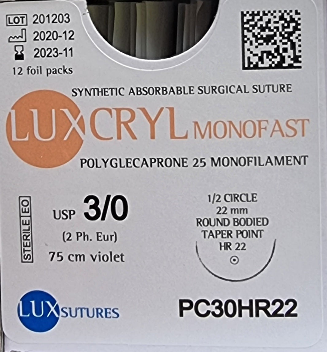 A close-up view of a box of Luxcryl Monofast synthetic absorbable surgical sutures. The label specifies USP 3/0 (2 Ph. Eur.), a 1/2 circle round-bodied taper point needle (22mm), and a 75cm violet suture length. The sutures are made of poliglecaprone 25 monofilament, with the lot number, manufacturing, and expiration dates clearly visible.