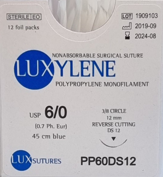 A close-up view of a box of Luxylene polypropylene monofilament surgical sutures, labeled as USP 6/0 (0.7 Ph. Eur.), with a 3/8 circle reverse cutting needle (12mm) and a 45cm blue suture length. The packaging indicates it is non-absorbable, sterile, and contains 12 foil packs, with the lot number and expiry date clearly visible.