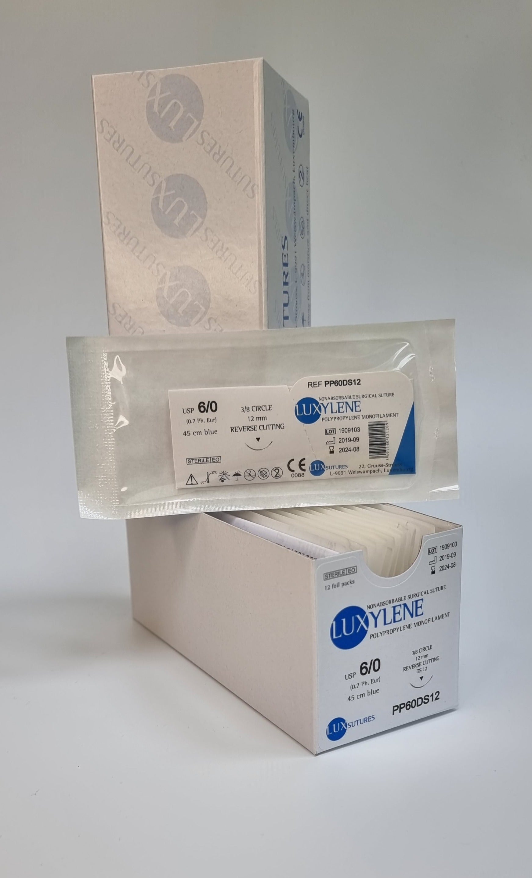 A box of Luxylene polypropylene monofilament surgical sutures is shown, with one individually packed suture displayed in front. The label specifies USP 6/0 (0.7 Ph. Eur.), 45cm blue suture, and a 12mm reverse cutting needle. The packaging is white with blue branding, and the product is intended for surgical use. The background is plain, emphasizing the sterile packaging.